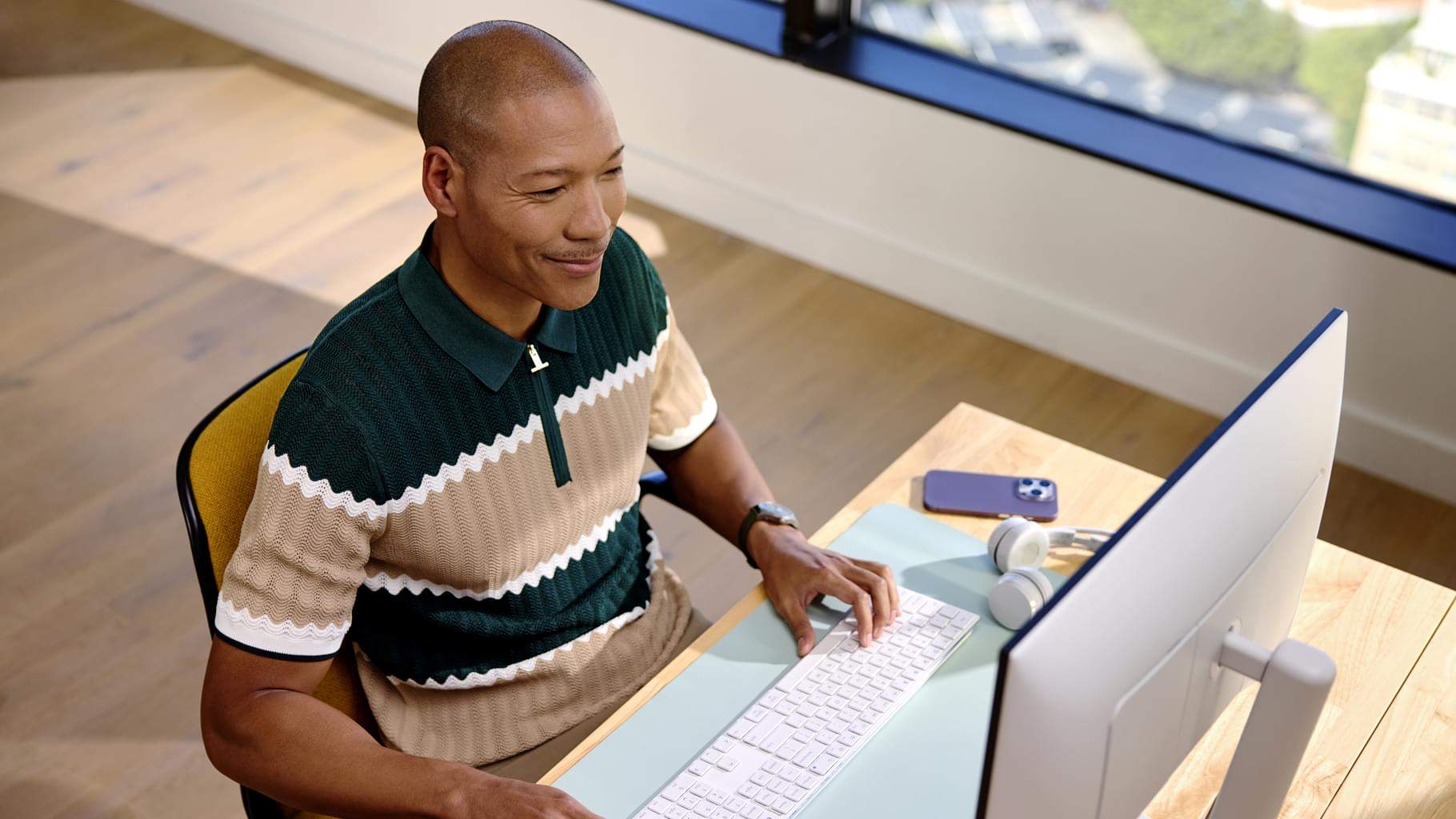 A man sitting at a desk, looking at a computer and smiling. 