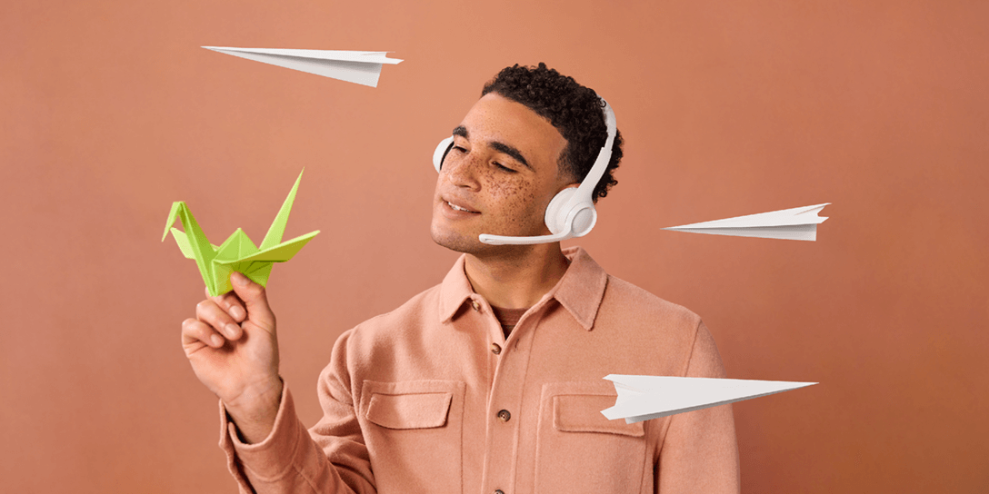 A person holds a green folded paper crane as paper planes fly through the air.