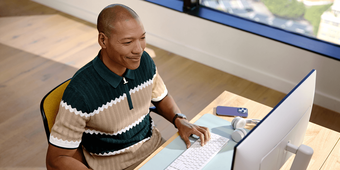 A smiling person in a striped polo shirt works at a computer, demonstrating effective IT asset management.