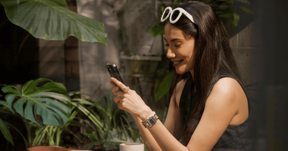 A woman in sunglasses is engaged with her smartphone, sending a message.