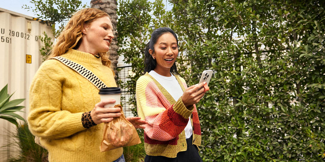 Two women walking while looking at a phone 