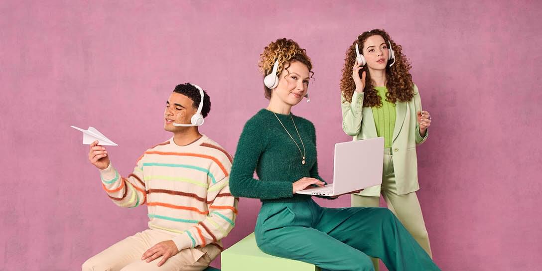 Three individuals wear headsets with one sitting holding a paper airplane, one sitting with a laptop, and one standing.