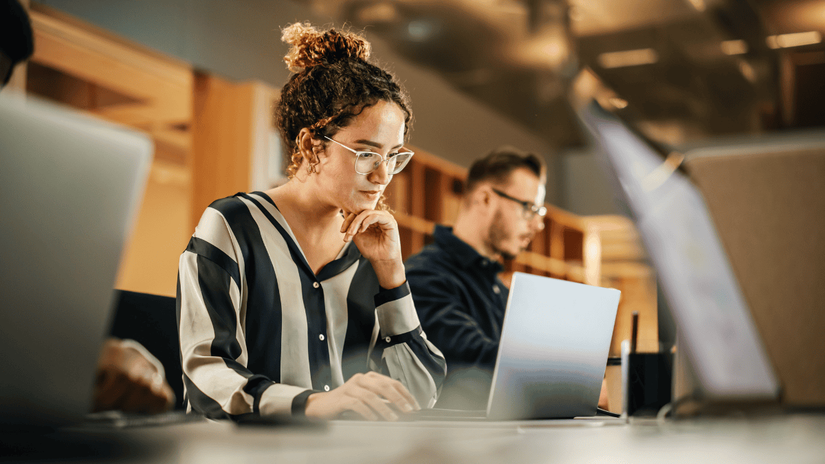 Woman wearing glasses learning about outcomes-based pricing on a laptop in a modern office.