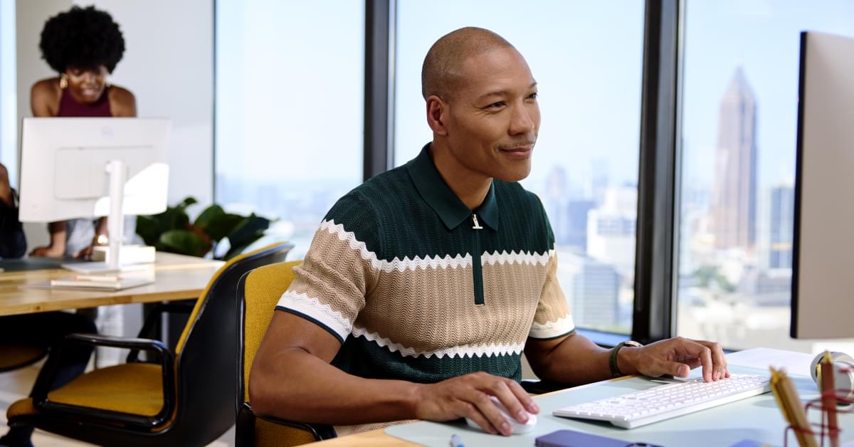 A man sitting in an office, at a desk, using a computer to work on AI innovations in customer service.