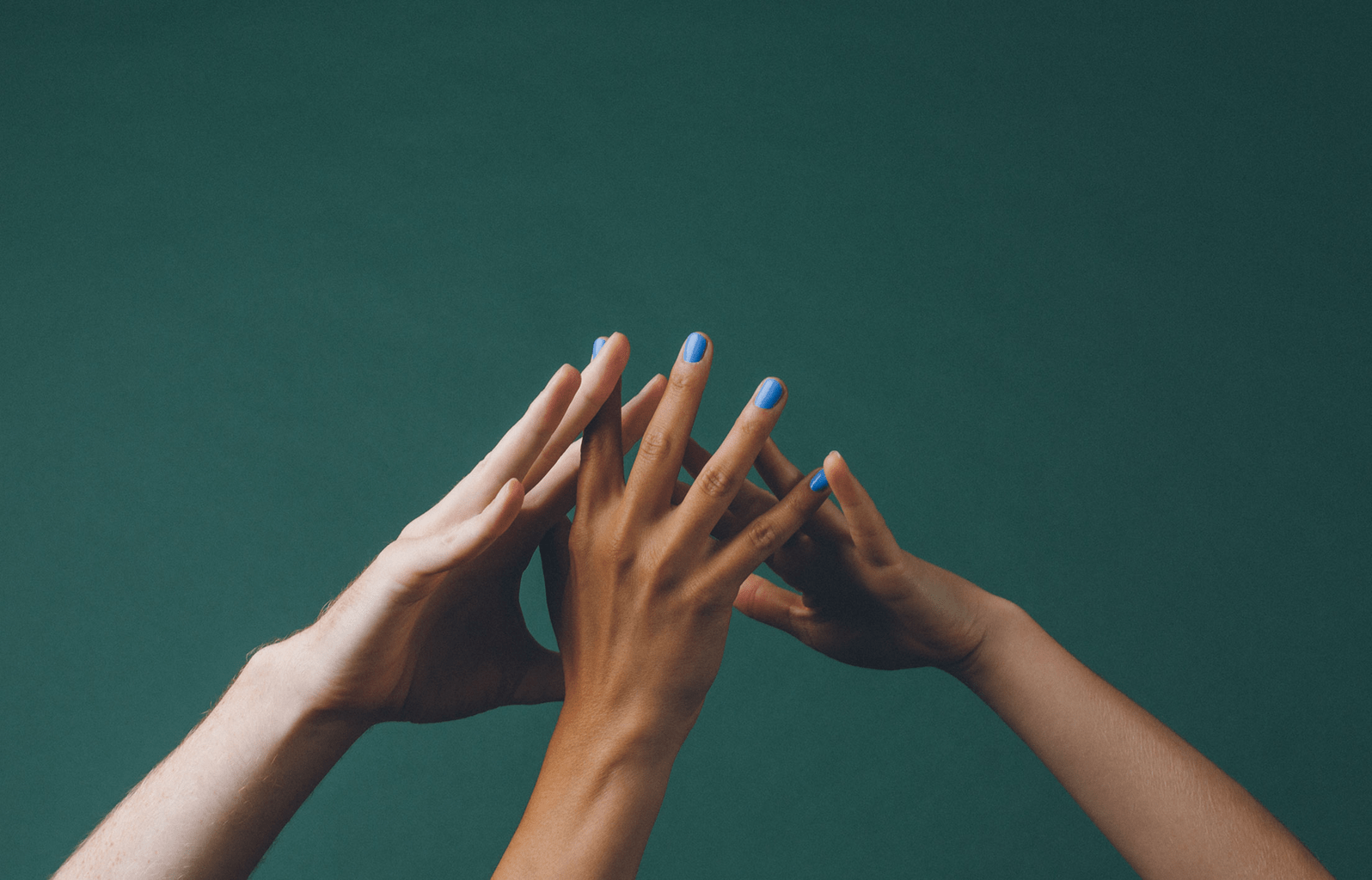 Three people holding up their hands together in a huddle as if to demonstrate teamwork