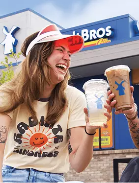 Two women sitting out front of a Dutch Bros cafe holding coffee and tea